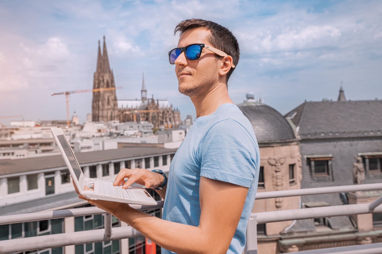 Ein Mann tippt auf einer Dachterrasse in der Kölner Innenstadt auf einem Notebook, im Hintergrund der Dom